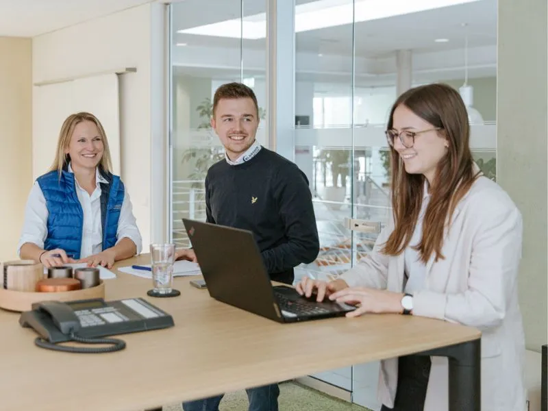 Bild mit 2 Frauen und einem Mann am Bürotisch in einer Besprechung mit Laptop